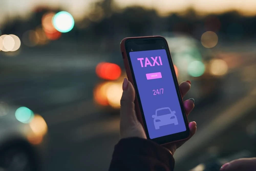 main d'une femme tenant un smartphone avec une application de réservation de taxi ouverte