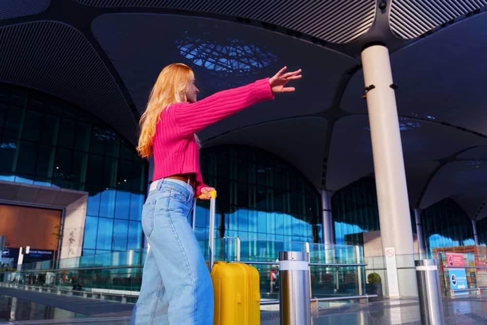 jeune femme blonde avec une valise hélant un taxi à l'aéroport de Bordeaux