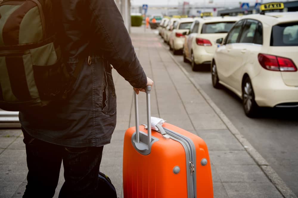 homme avec une valise et des sacs attendant un taxi à la sortie d'un aéroport